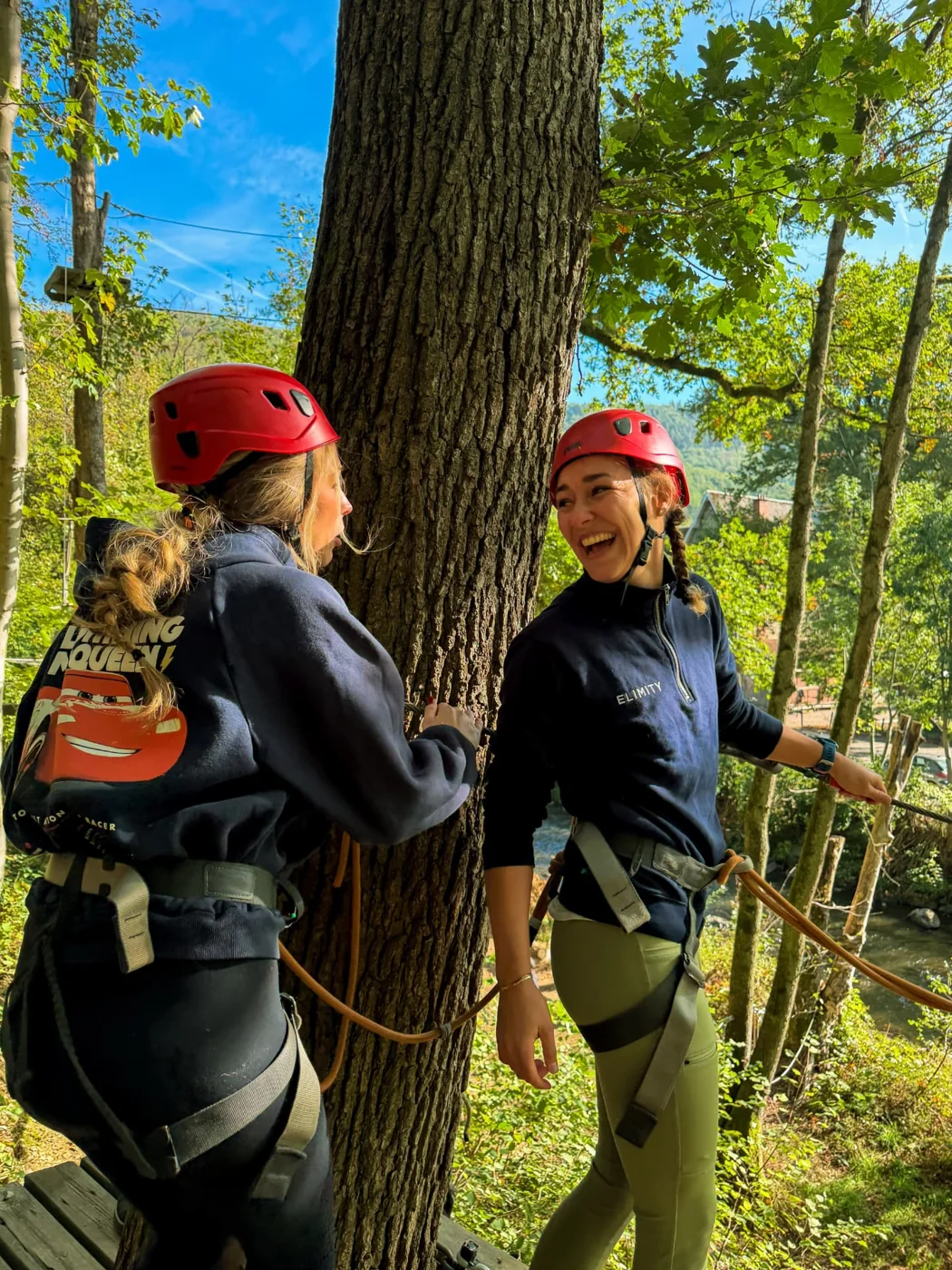 Two Elimity teammates laughing together on a treetop ropes course